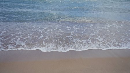 Eine ruhige Strandszene fängt das sanfte Plätschern schäumender Wellen im sonnenverwöhnten Sand ein