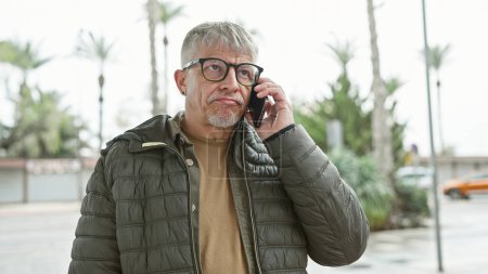 Photo for A middle-aged man with grey hair talking on a smartphone on a city street. - Royalty Free Image