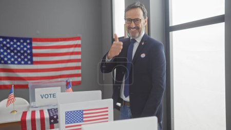 Téléchargez les photos : Un homme mûr barbu avec un pouce levé dans un cadre de collège électoral américain orné de drapeaux. - en image libre de droit