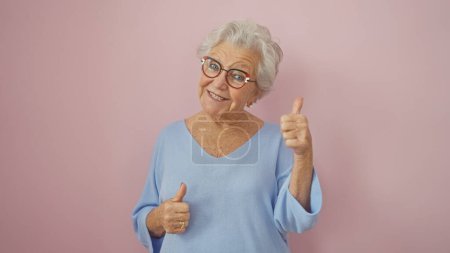 Photo for Smiling senior woman giving thumbs up against a pink background, portraying positivity and approval. - Royalty Free Image