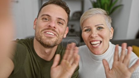 Un hombre y una mujer alegres sonriendo y saludando a la cámara en un interior de salón moderno bien iluminado