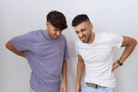 Téléchargez les photos : Couple homosexuel gay debout sur fond blanc souffrant de maux de dos, toucher le dos avec la main, douleur musculaire - en image libre de droit