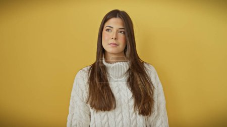 Foto de Retrato de una hermosa joven hispana en un suéter blanco posando sobre un fondo amarillo aislado. - Imagen libre de derechos