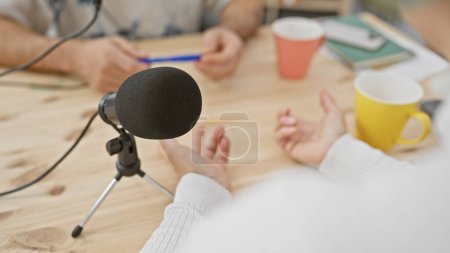 Téléchargez les photos : Un homme et une femme participant à une séance d'enregistrement de podcast d'intérieur avec un microphone sur une table en bois - en image libre de droit
