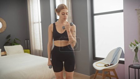 Téléchargez les photos : Une jeune femme fait des exercices avec des haltères dans une chambre moderne, mettant en évidence la forme physique et un mode de vie sain à la maison. - en image libre de droit