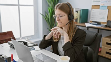 Foto de Una joven profesional que usa auriculares se concentra mientras trabaja en su computadora portátil en una oficina moderna. - Imagen libre de derechos
