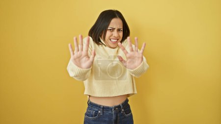 Junge hispanische Frau mit negativer Geste vor gelbem Hintergrund zeigt Ablehnung.