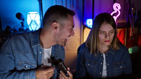 Ein Paar in einem Spielzimmer, wo der aufgeregte Mann mit Controller und die fokussierte Frau nachts auf den Bildschirm starren.
