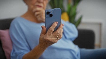 Téléchargez les photos : Femme âgée dans un salon en utilisant judicieusement smartphone - en image libre de droit