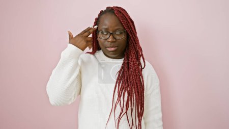 Téléchargez les photos : Femme noire adulte avec des tresses et des lunettes posant sur un fond rose, exprimant sa réflexion. - en image libre de droit