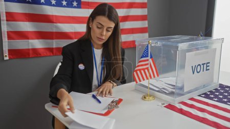 Una joven hispana que trabaja en un centro electoral americano con una bandera de fondo