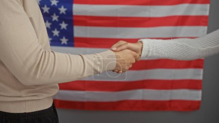 Two people shaking hands in an office with an american flag background symbolizing partnership and professionalism in the usa.