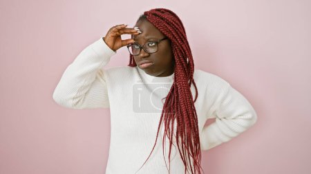 Foto de Mujer afroamericana reflexiva con trenzas con gafas y suéter blanco sobre un fondo rosa. - Imagen libre de derechos