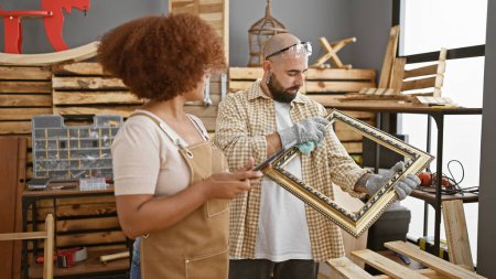 Deux menuisiers professionnels dans un atelier de menuiserie vintage, nettoyant un cadre antique avec un pavé tactile à l'atelier de menuiserie