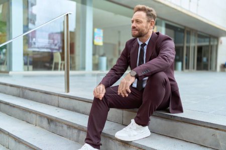 Téléchargez les photos : Homme d'âge moyen travailleur d'affaires assis sur les escaliers avec une expression détendue dans la rue - en image libre de droit