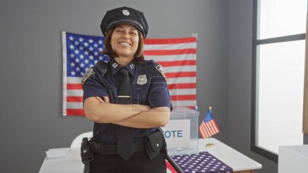 Téléchargez les photos : Une policière souriante aux bras croisés se tient devant un drapeau américain dans un centre de vote, symbolisant la sécurité électorale. - en image libre de droit