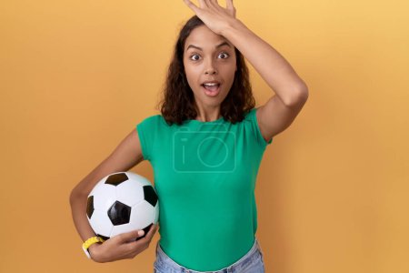 Photo for Young hispanic woman holding ball surprised with hand on head for mistake, remember error. forgot, bad memory concept. - Royalty Free Image