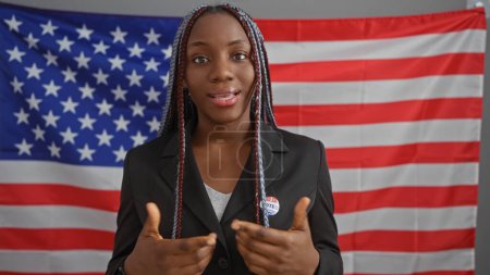 Téléchargez les photos : Femme afro-américaine avec des tresses en tenue de travail avec un autocollant "j'ai voté" devant le drapeau US dans un bureau. - en image libre de droit