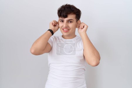 Photo for Young non binary man wearing casual white t shirt smiling pulling ears with fingers, funny gesture. audition problem - Royalty Free Image