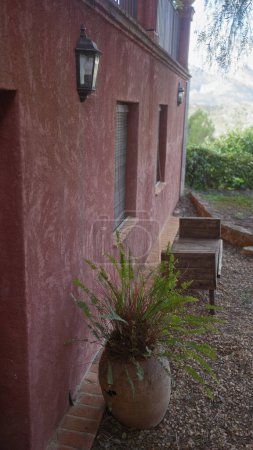Eine ruhige, terrakottafarbene Hacienda-Mauer mit einer hängenden Laterne und eingetopftem Farn an einem Kiesweg.