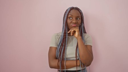 Photo for Pensive african woman with braids against isolated pink background, portraying casual beauty. - Royalty Free Image