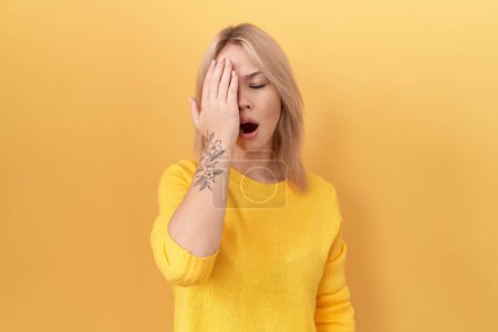 Foto de Mujer joven caucásica con suéter amarillo bostezando cansada cubriendo media cara, ojo y boca con la mano. cara duele en el dolor. - Imagen libre de derechos