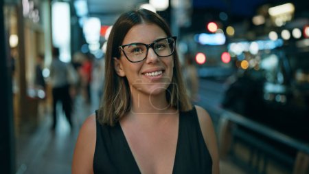 Photo for Laughing out loud, a confident beautiful hispanic woman wearing glasses stands joyfully on a street in kyoto, light-filled japanese city at night, looking positively radiant and carefree - Royalty Free Image