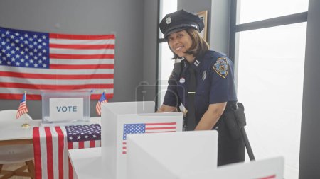 Téléchargez les photos : Une policière souriante supervisant un bureau de vote avec des isoloirs, des drapeaux américains et une urne à l'intérieur. - en image libre de droit