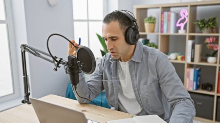 Foto de Hombre hispano podcasting con micrófono y auriculares en una configuración de estudio en casa - Imagen libre de derechos