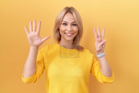 Téléchargez les photos : Jeune femme caucasienne portant un pull jaune montrant et pointant vers le haut avec les doigts numéro huit tout en souriant confiant et heureux. - en image libre de droit