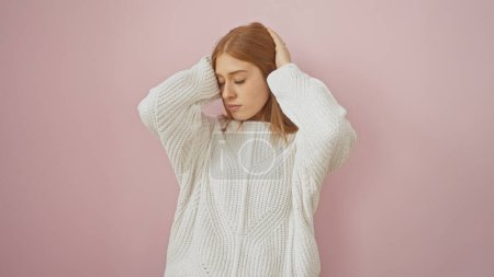 Foto de Una joven, hermosa mujer caucásica con el pelo rojo, se encuentra en una pose relajada sobre un fondo rosa aislado, evocando una sensación de calma y simplicidad. - Imagen libre de derechos