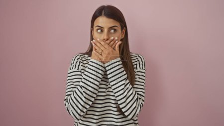 Surprised young woman with hand over mouth against a pink isolated background wearing a striped shirt.