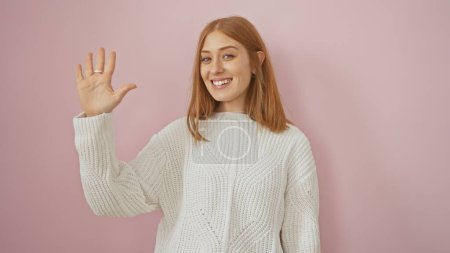 Foto de Una joven pelirroja con un suéter blanco hace cinco gestos sobre un fondo rosa, retratando un ambiente amistoso y casual. - Imagen libre de derechos