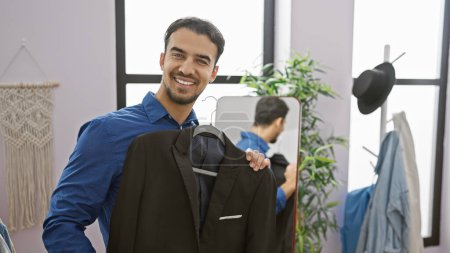 Foto de Hombre hispano guapo sonriendo sujetando traje en un armario moderno - Imagen libre de derechos
