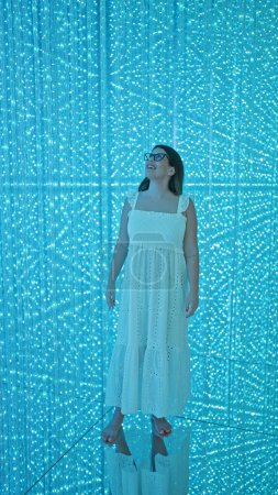 Smiling beautiful hispanic woman in glasses experiences futuristic light exhibition at modern museum, an immersive art exhibit sparking creativity and happiness
