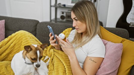 A woman on a couch using a smartphone with a small dog beside her, indoors, at home, comfortable, casual