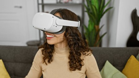 Photo for Smiling woman using virtual reality headset in modern living room, experiencing immersive technology indoors. - Royalty Free Image