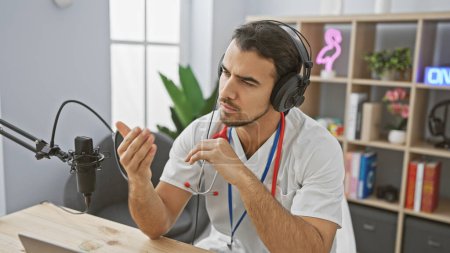 Foto de Hombre hispano guapo usando auriculares hablando en un micrófono en un moderno ambiente de estudio interior - Imagen libre de derechos