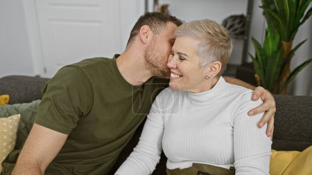 Ein Mann und eine Frau küssen sich liebevoll auf die Wange, während sie es sich auf einem Sofa in einem gemütlichen Innenraum gemütlich machen