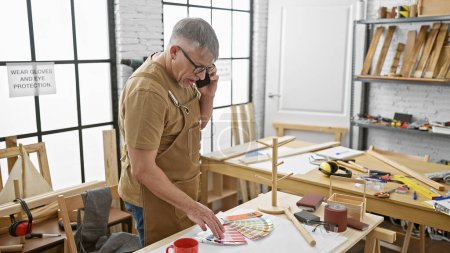 Photo for Mature man discussing woodworking plans over the phone in an organized workshop. - Royalty Free Image