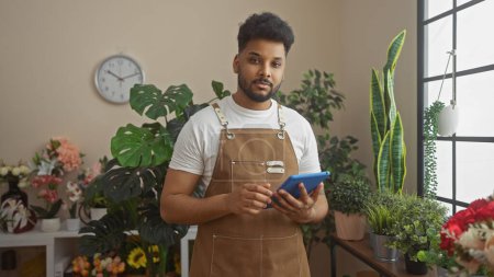 A handsome man with a tablet managing a lush flower shop adorned with a variety of plants and bouquets.
