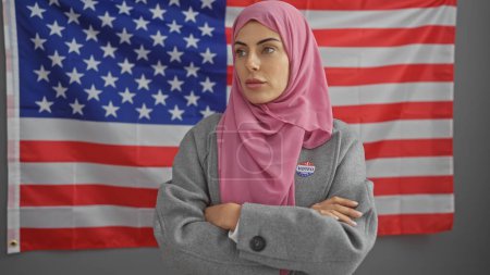 A young woman in a hijab with a 'voted' sticker stands before an american flag, implying civic participation.