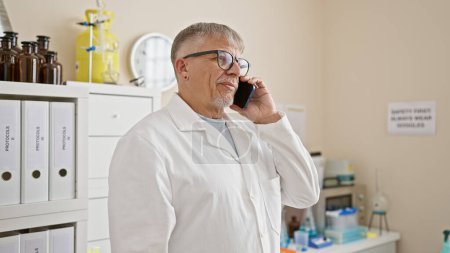 Mature man wearing glasses and lab coat talking on phone in a laboratory setting