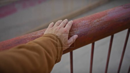 Téléchargez les photos : Une main d'homme saisissant une balustrade rouillée sur un pont à l'extérieur, représentant la décomposition urbaine et la négligence. - en image libre de droit