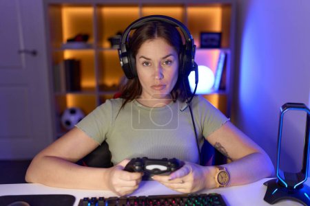 Photo for Beautiful brunette woman playing video games wearing headphones relaxed with serious expression on face. simple and natural looking at the camera. - Royalty Free Image