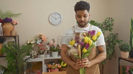 Handsome man holding colorful tulips in a green indoor flower shop with blurred floral background.