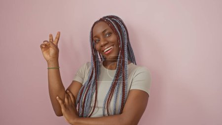 Foto de Mujer negra adulta con trenzas haciendo señal de victoria sobre un fondo rosa aislado, retrato de belleza y confianza. - Imagen libre de derechos