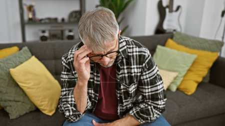 Photo for Mature grey-haired man in glasses feeling stressed seated on a couch indoors - Royalty Free Image