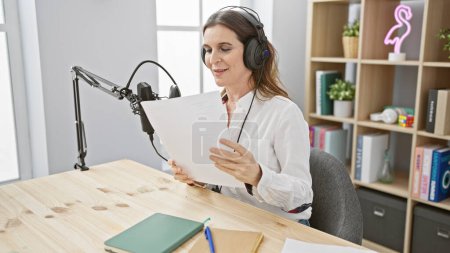 Mujer de mediana edad con auriculares en estudio de podcast leyendo un guion.