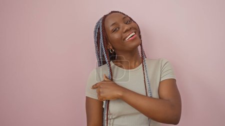 Foto de Una alegre mujer afroamericana con trenzas posa sobre un fondo rosa aislado, evocando belleza y confianza. - Imagen libre de derechos
